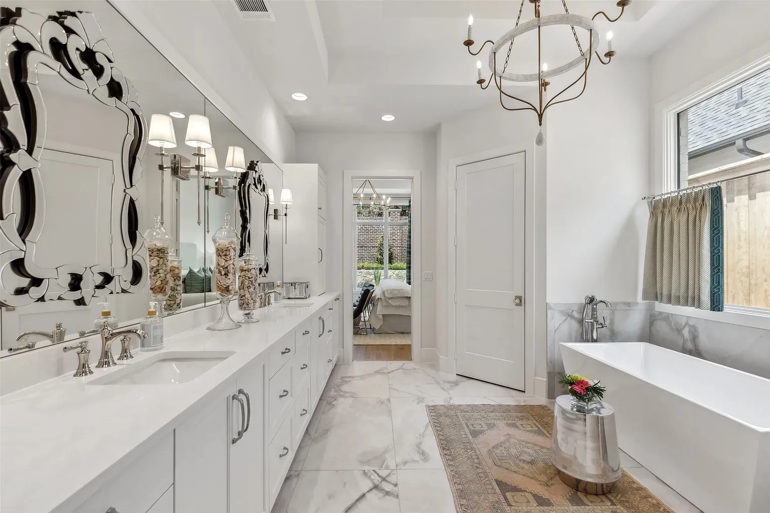 Luxurious white master bathroom with marble floors, double vanity, ornate mirror, and freestanding bathtub