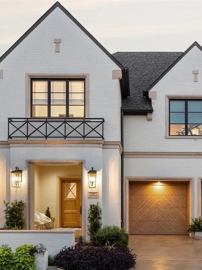 Modern white brick house exterior with gable roof, wooden garage door, and black-framed windows