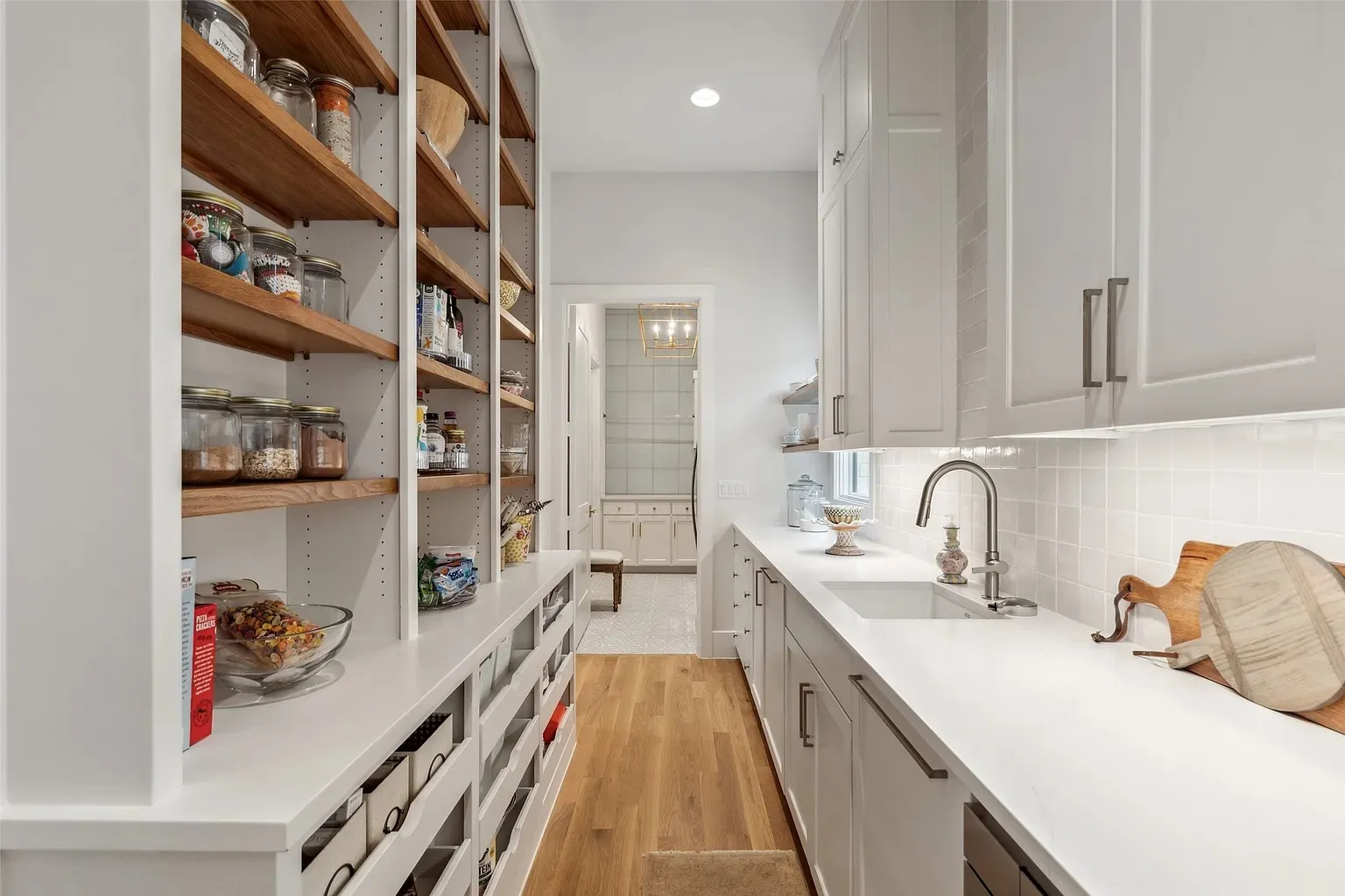 Spacious walk-in pantry with open wooden shelving, white cabinetry, and quartz countertops